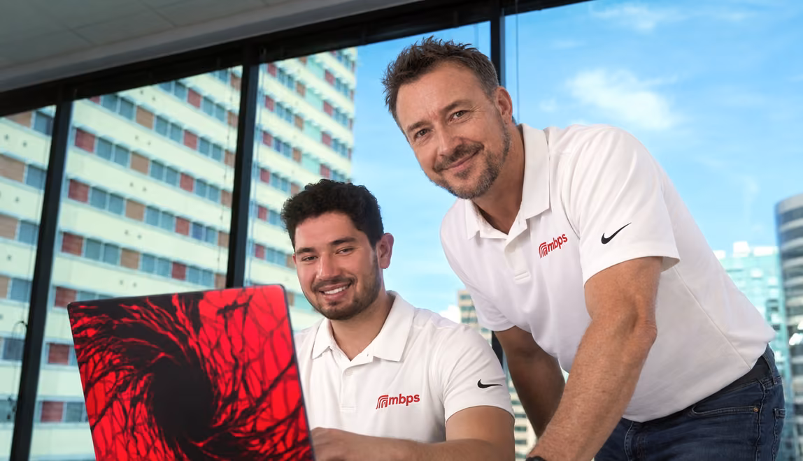 Two MBPS colleagues at a laptop with a city view behind them