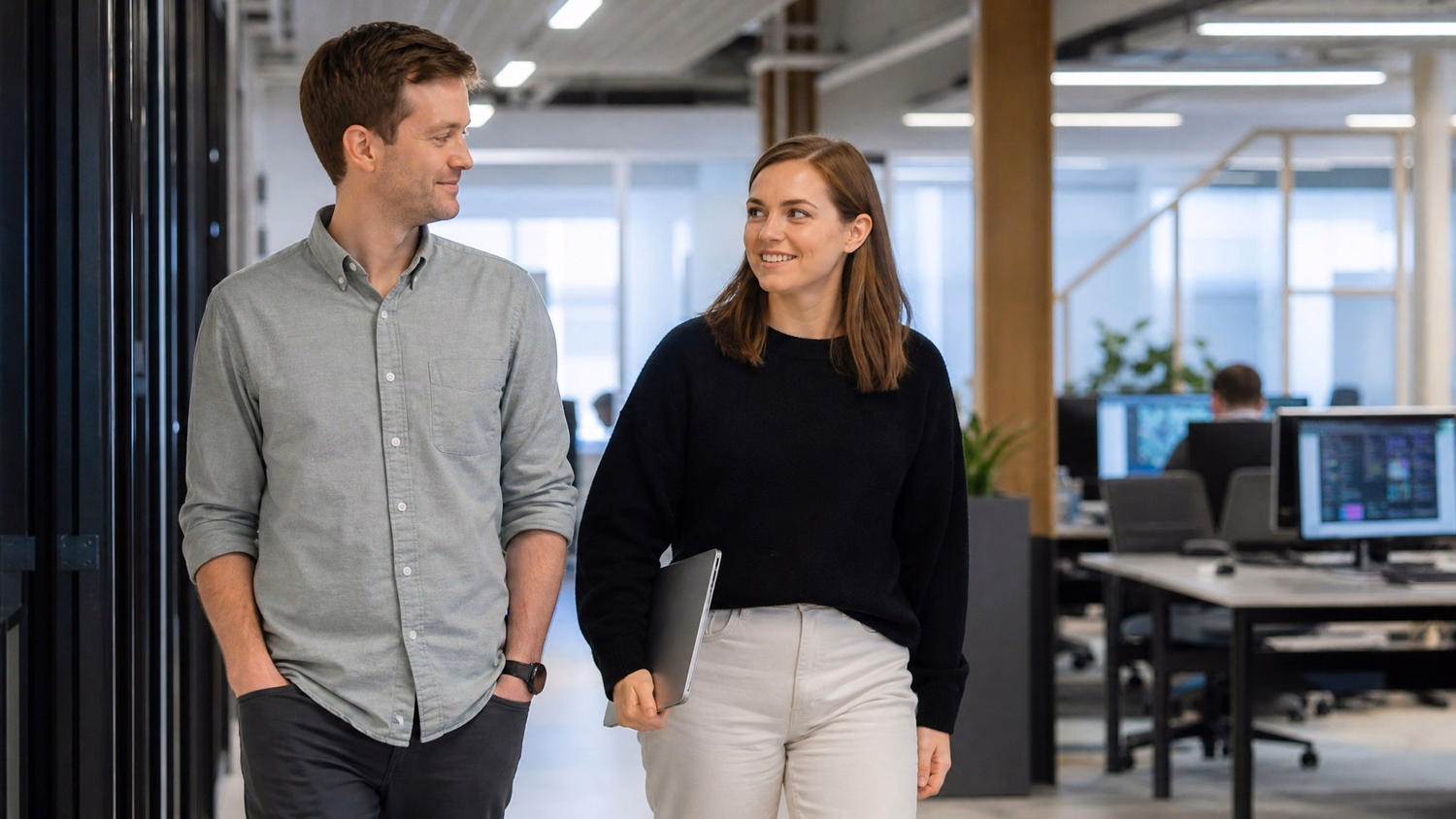 Two colleagues walk and talk in bright office hallway