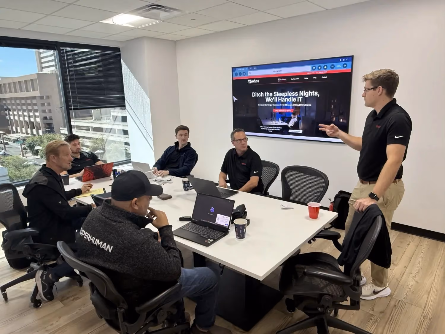 MBPS presenter addressing staff in a conference room with a city view