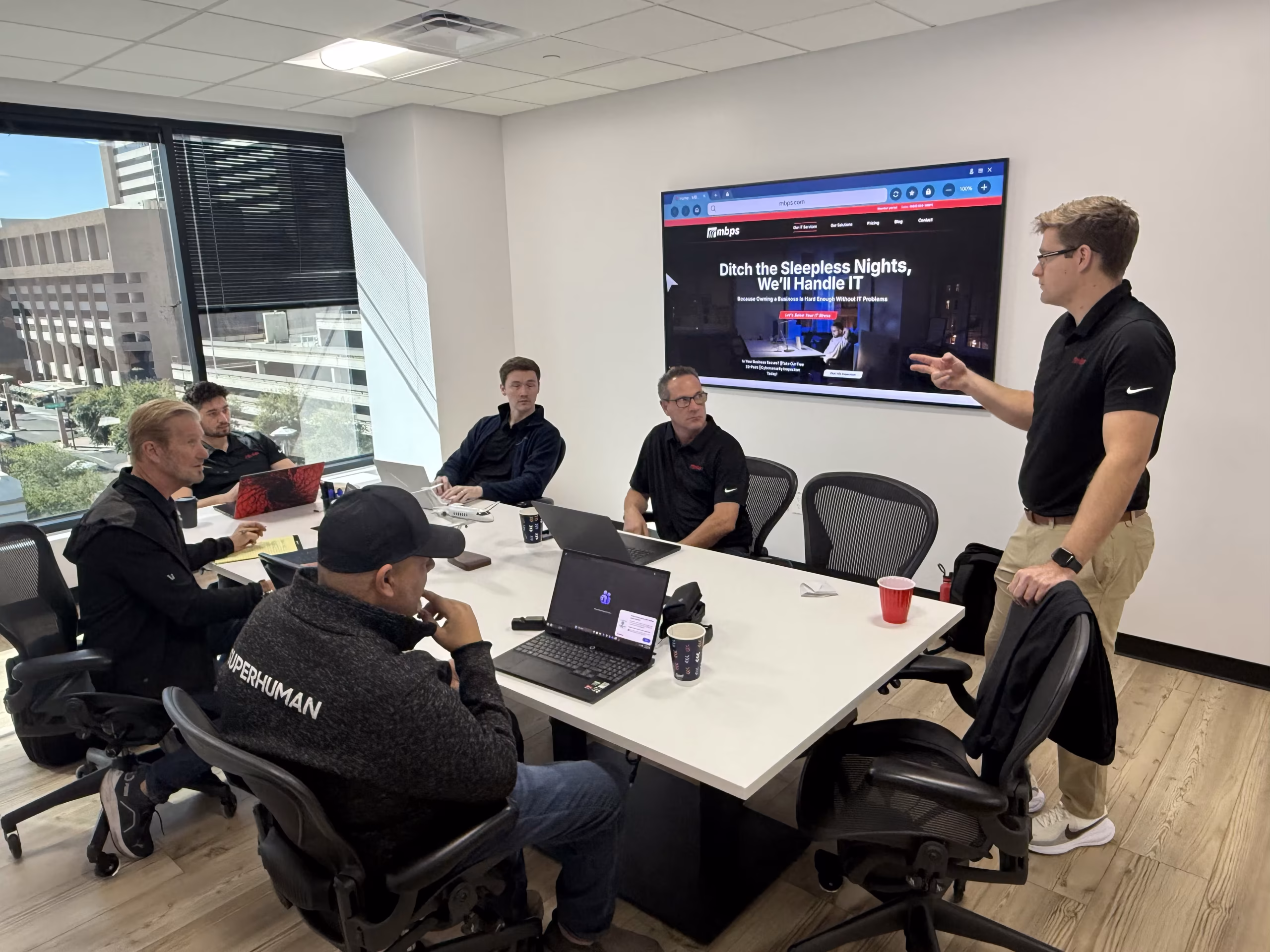 MBPS staff meeting with a presenter beside a wall screen in the Phoenix office